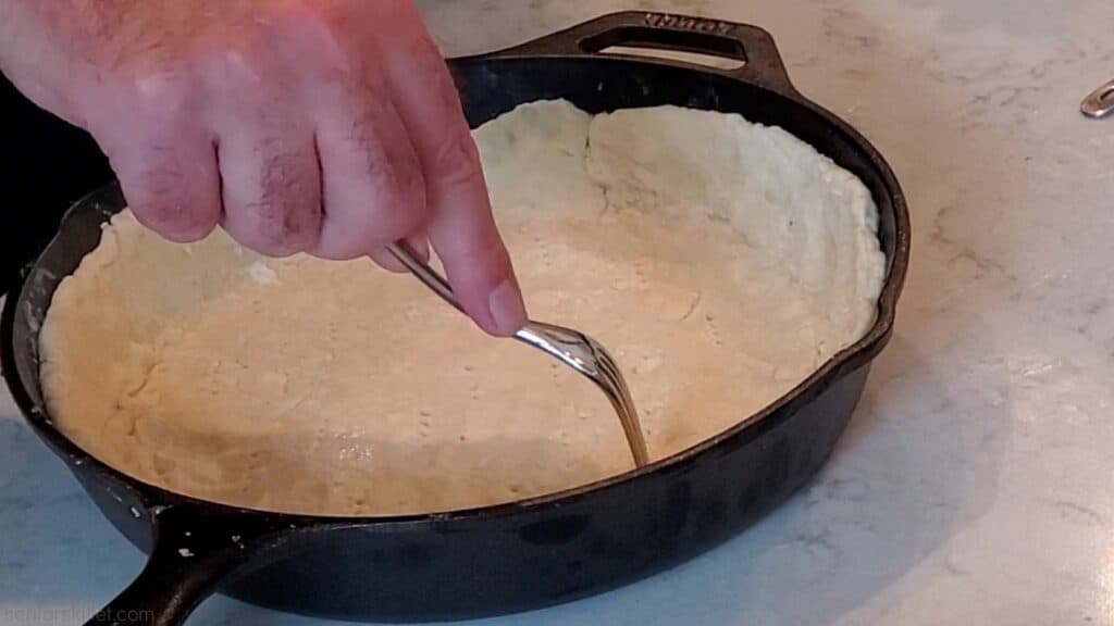 Pie crust being poked with fork