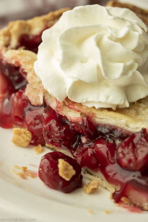 Slice of cherry pie on a plate with whipped cream
