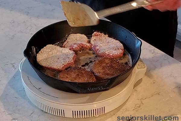 Using a spatula to turn cube steaks in a pan